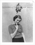 1930s 1940s cute young woman standing under mistletoe smiling hand near mouth looking at camera by Anonymous