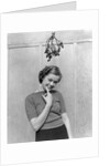 1930s 1940s cute young woman standing under mistletoe smiling hand near mouth looking at camera by Anonymous