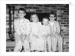 Siblings perch on a hearth in pajamas, ca. 1970. by Anonymous