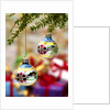 Close-up of decorated hanging baubles against blurred gifts in the background by Anonymous