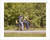 1970s Family On Tandem Bicycle Mother Father Son & Baby Daughter In Backpack Wearing Bellbottom Blue Jeans Looking At Camera by Anonymous