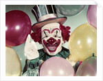 1950s Circus Clown Portrait Smiling Amid Balloons Pointing Up Looking At Camera by Anonymous