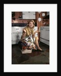 1960s Young Smiling Blond Housewife Sitting On Top Of Laundry Basket Kitchen by Anonymous
