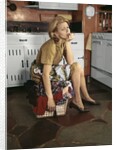1960s Tired Housewife Sitting On Top Of Laundry Basket In Kitchen by Anonymous