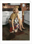 1960s Tired Housewife Sitting On Top Of Laundry Basket In Kitchen by Anonymous