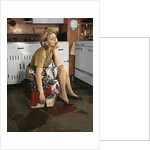 1960s Tired Housewife Sitting On Top Of Laundry Basket In Kitchen by Anonymous