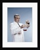 1960s Man Wearing Lab Coat Pouring Liquid From Small Erlenmeyer Flask Into A Larger Flask by Anonymous
