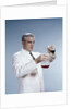 1960s Man Wearing Lab Coat Pouring Liquid From Small Erlenmeyer Flask Into A Larger Flask by Anonymous