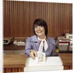 1970s Smiling Woman Bank Teller Handing Cash Over Counter by Anonymous