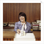 1970s Smiling Woman Bank Teller Handing Cash Over Counter by Anonymous