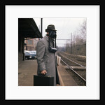 1950s Man Wearing Gas Mask Hat At Commuter Train Station Holding Briefcase Newspaper by Anonymous