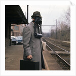 1950s Man Wearing Gas Mask Hat At Commuter Train Station Holding Briefcase Newspaper by Anonymous