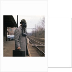 1950s Man Wearing Gas Mask Hat At Commuter Train Station Holding Briefcase Newspaper by Anonymous
