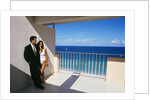 1990s Man In Dark Suit And Tie And Woman In White One Piece Bathing Suit Standing Together On Ocean Side Sun Deck by Anonymous