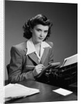 1940s Serious Secretary Stenographer Woman With Pencil Checking Notepad Sitting At Desk With Manual Typewriter Looking At Camera by Anonymous