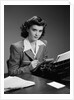 1940s Serious Secretary Stenographer Woman With Pencil Checking Notepad Sitting At Desk With Manual Typewriter Looking At Camera by Anonymous