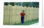 1980s Smiling Boy Running Along Sidewalk Rattling Stick On Tall Picket Fence Making Noise by Anonymous