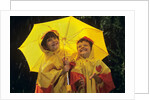 1990s Two Laughing Young Girls Holding A Yellow Umbrella And Wearing Yellow Rain Ponchos by Anonymous