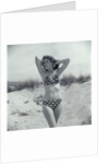 1950s Brunette Bathing Beauty In Polka Dot Bikini Standing In Sand With Hands Behind Head Looking At Camera by Anonymous