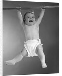 1960s Baby Hanging From Rod With Frightened Expression On Verge Of Tears by Anonymous