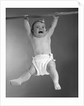 1960s Baby Hanging From Rod With Frightened Expression On Verge Of Tears by Anonymous