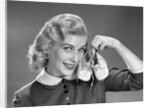 1950s 1960s Smiling Blond Woman Communicating That She Is Mother To Be By Holding Up A Pair Of Baby Shoes Looking At Camera by Anonymous