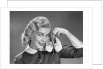 1950s 1960s Smiling Blond Woman Communicating That She Is Mother To Be By Holding Up A Pair Of Baby Shoes Looking At Camera by Anonymous