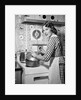 1950s Housewife Wearing Checkered Dress Standing In Kitchen Stirring Pot On Stove Looking Over Shoulder by Anonymous