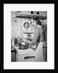 1950s Housewife Wearing Checkered Dress Standing In Kitchen Stirring Pot On Stove Looking Over Shoulder by Anonymous