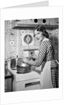 1950s Housewife Wearing Checkered Dress Standing In Kitchen Stirring Pot On Stove Looking Over Shoulder by Anonymous