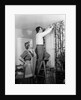 1950s Skeptical Wife In Apron Fingers Pressing Chin Watching Husband On Ladder Hanging New Jungle Motif Drapes In Living Room by Anonymous