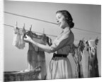 1950s Smiling Woman Housewife Hanging Wash Child Dress On Clothesline To Dry by Anonymous