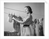 1950s Smiling Woman Housewife Hanging Wash Child Dress On Clothesline To Dry by Anonymous