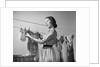1950s Smiling Woman Housewife Hanging Wash Child Dress On Clothesline To Dry by Anonymous