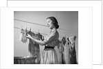 1950s Smiling Woman Housewife Hanging Wash Child Dress On Clothesline To Dry by Anonymous