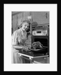 1950s Smiling Woman Housewife Wearing Apron Taking Large Roast Beef From Electric Oven In Kitchen Looking At Camera by Anonymous