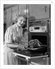 1950s Smiling Woman Housewife Wearing Apron Taking Large Roast Beef From Electric Oven In Kitchen Looking At Camera by Anonymous