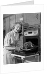 1950s Smiling Woman Housewife Wearing Apron Taking Large Roast Beef From Electric Oven In Kitchen Looking At Camera by Anonymous
