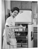 1950s Smiling Woman Housewife Putting Stick Of Butter Into Electric Refrigerator In Kitchen Looking At Camera by Anonymous