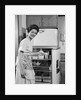 1950s Smiling Woman Housewife Putting Stick Of Butter Into Electric Refrigerator In Kitchen Looking At Camera by Anonymous