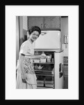 1950s Smiling Woman Housewife Putting Stick Of Butter Into Electric Refrigerator In Kitchen Looking At Camera by Anonymous