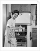 1950s Smiling Woman Housewife Putting Stick Of Butter Into Electric Refrigerator In Kitchen Looking At Camera by Anonymous