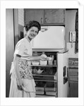 1950s Smiling Woman Housewife Putting Stick Of Butter Into Electric Refrigerator In Kitchen Looking At Camera by Anonymous