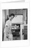 1950s Smiling Woman Housewife Putting Stick Of Butter Into Electric Refrigerator In Kitchen Looking At Camera by Anonymous