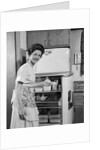 1950s Smiling Woman Housewife Putting Stick Of Butter Into Electric Refrigerator In Kitchen Looking At Camera by Anonymous