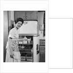 1950s Smiling Woman Housewife Putting Stick Of Butter Into Electric Refrigerator In Kitchen Looking At Camera by Anonymous
