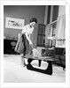 1950s 1960s Woman Wearing A White Blouse & Plaid Skirt Dusting With A Feather Duster A Glass Top Coffee Table by Anonymous