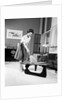 1950s 1960s Woman Wearing A White Blouse & Plaid Skirt Dusting With A Feather Duster A Glass Top Coffee Table by Anonymous
