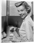 1950s Smiling Blonds Woman Mother Warming A Baby Bottle Of Milk In Kitchen Looking At Camera by Anonymous