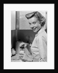 1950s Smiling Blonds Woman Mother Warming A Baby Bottle Of Milk In Kitchen Looking At Camera by Anonymous